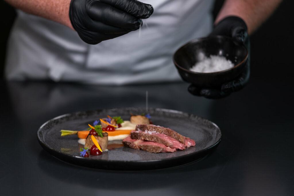 Sustainable cuisine at STURM – chef wearing gloves salts a plate of organic meat