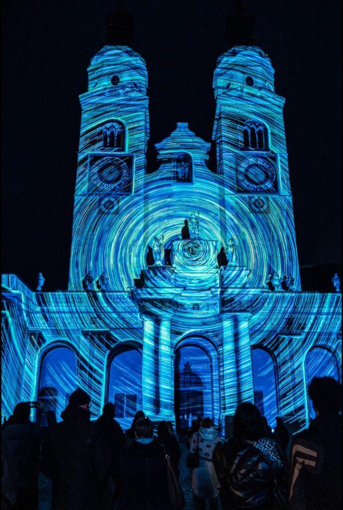 The church in Brixen is illuminated with lights. A crowd gathers to watch during the Water Light Festival