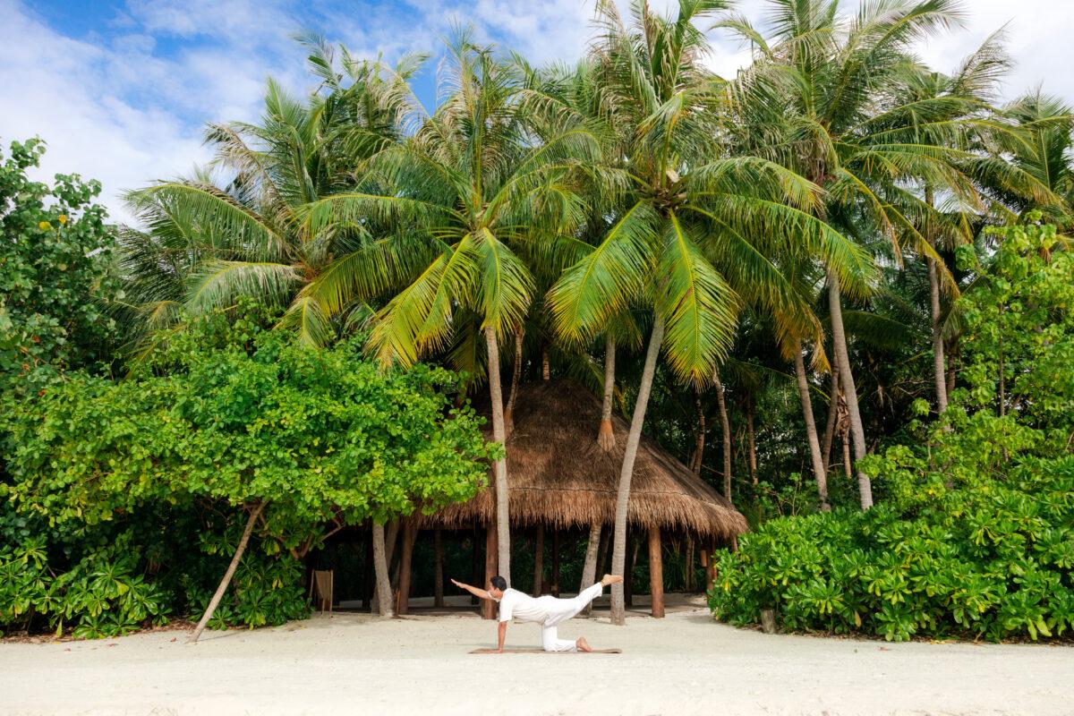 Man in a yoga pose on the beach under palm trees in the Maldives