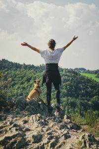 junge Frau steht mit Hund auf Felsen und vermittelt einGefühl von Freiheit