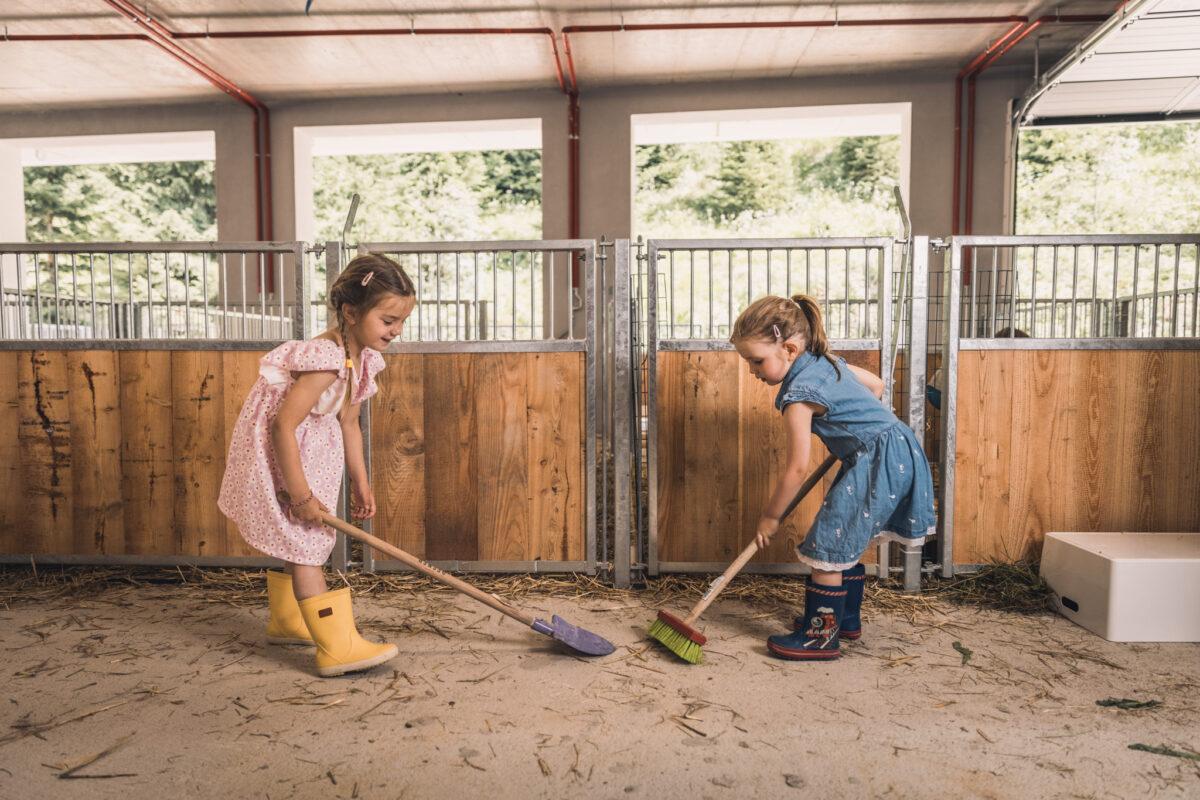 Two girls cleaning the stable at the petting zoo of the sustainable Hotel Klosterbräu in Seefeld.