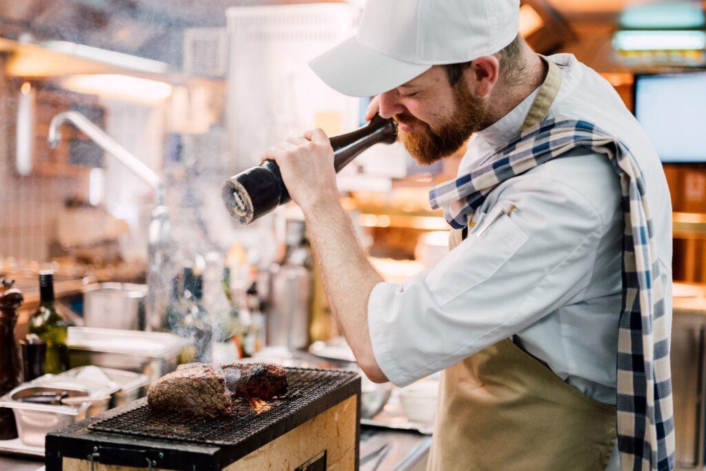 A chef at the Stanglwirt seasons the meat with a large pepper mill in the kitchen