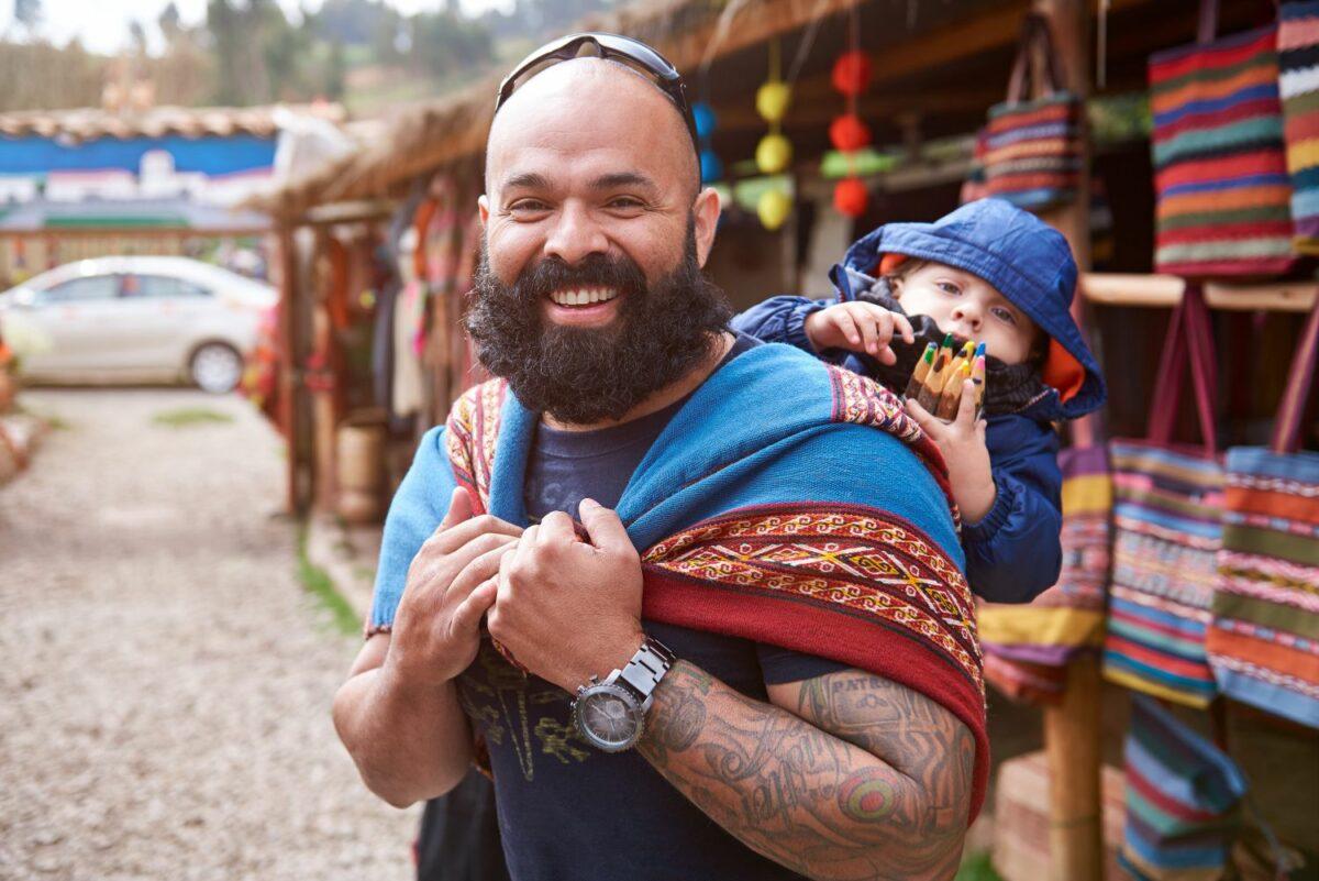 Man in Peru carrying a small child in a baby carrier.