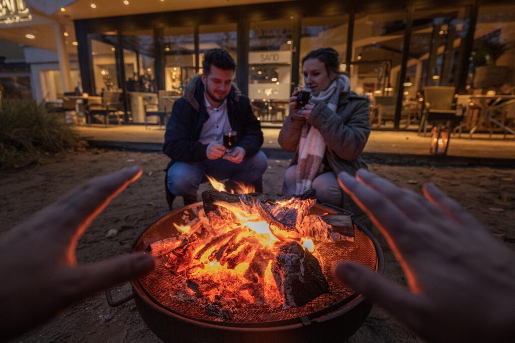 Couple sitting by the fire pit in front of the Lifestylehotel SAND with its sustainable lifestyle on the Baltic Sea
