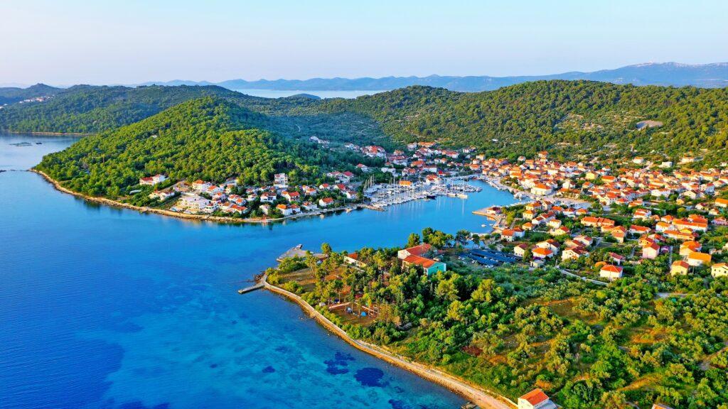 Luftaufnahme der Insel Iz in Kroatien mit bunten Häusern, eingebettet zwischen üppig grünen Hügeln und einer klarblauen Bucht, die eine ruhige und malerische Atmosphäre vermittelt.