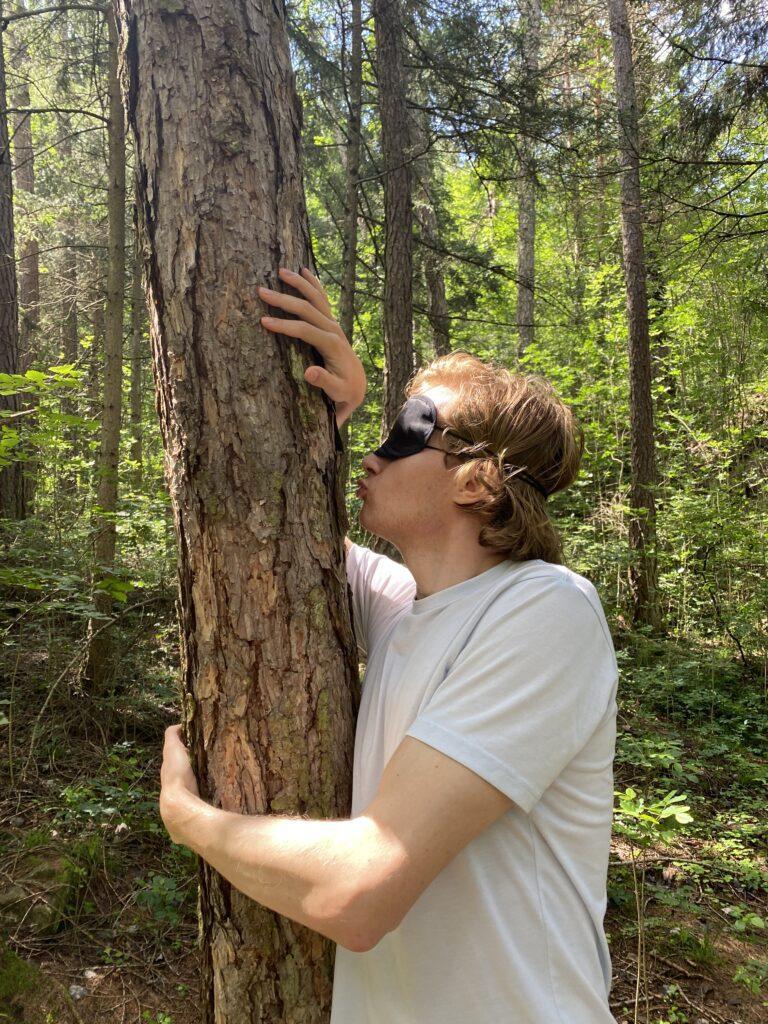Mann mit Augenmaske küsst einen Baum beim Waldbaden in Naturns Südtirol