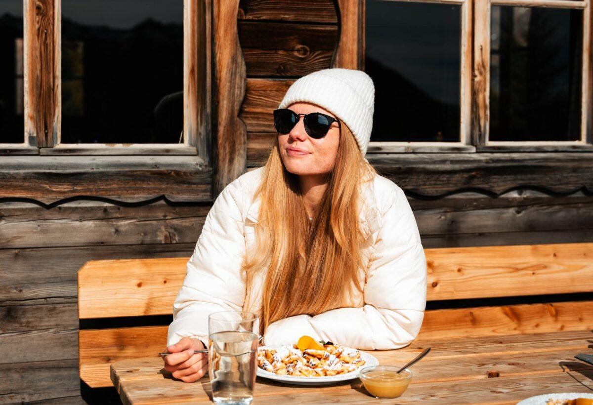 A woman is basking in the sunshine on the terrace of a mountain cabin.