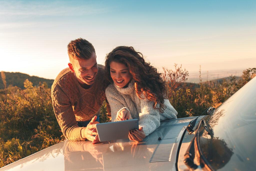 Beautiful couple on car trip, they take a break from driving and look for orientation on tablet.