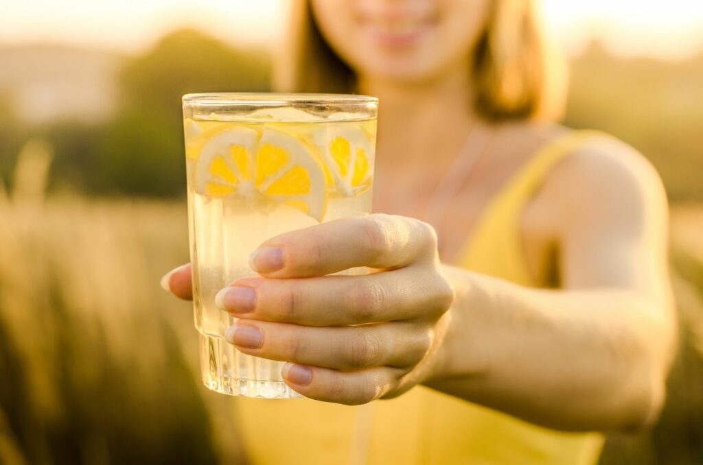 Woman with a glass of lemon water in the sun - Healthy & Happy