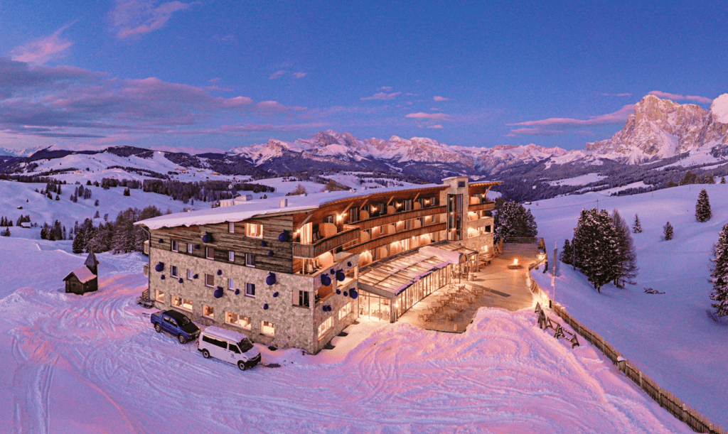 A sustainable ski-in, ski-out hotel at dusk with a view of the Dolomites.