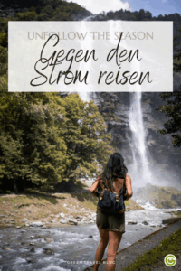 Zwei Personen gehen eine enge, von alten Gebäuden gesäumte Straße entlang, die von Pflanzen und Laternen belebt wird