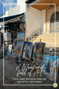 A street scene featuring several paintings lying on the ground and leaning against a wall, in front of a building with a staircase and a decorative entrance