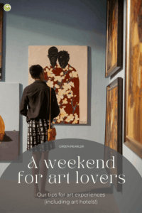 A person with short hair and a black top is looking at a painting of two people in floral clothing in a gallery with other framed pictures on the walls