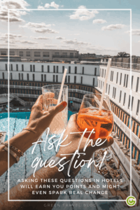 Two hands holding drinks with straws in front of a hotel building with a courtyard and pool