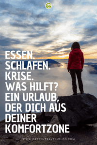 Eine Person mit roter Jacke steht auf einem Felsen und blickt auf eine wolkenverhangene Berglandschaft im Morgen- oder Abendlicht. Im Vordergrund ist großflächig weißer Text platziert: 'ESSEN. SCHLAFEN. KRISE. WAS HILFT? EIN URLAUB, DER DICH AUS DEINER KOMFORTZONE'.