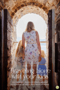 A view from behind of a woman in a white dress with a colorful pattern, looking out through a stone archway with two children