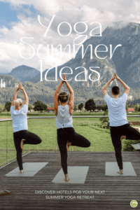 Three people are practicing yoga in the tree pose on yoga mats in front of a mountain landscape with meadows and trees